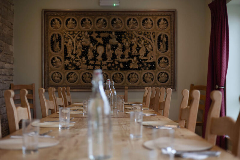 Dining Room of Florence House. Wooden table and chairs set for a meal with water bottle and glasses, plates and cutlery. Plus a wall hanging in gold and black