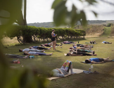 Yoga teacher standing in grounds of Florence House surrounded by her class lying on mats on the grass. The South Downs can be seen in the background